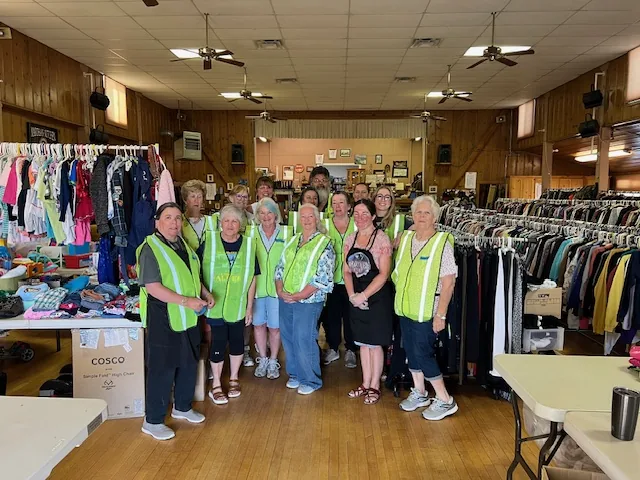 Inside Smith Valley Hall during the 2025 rummage sale: volunteers in yellow vests, clothing racks, ceiling fans and wood paneling.